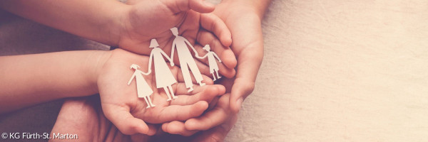 Eine aus Papier ausgeschnittene Familie wird von Händen gehalten